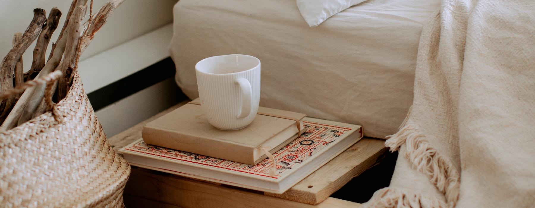 a white cup and books by the bedside